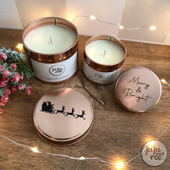 two spiced orange candles in rose gold tins; decorated with santa's sleigh and the words 'merry and bright'